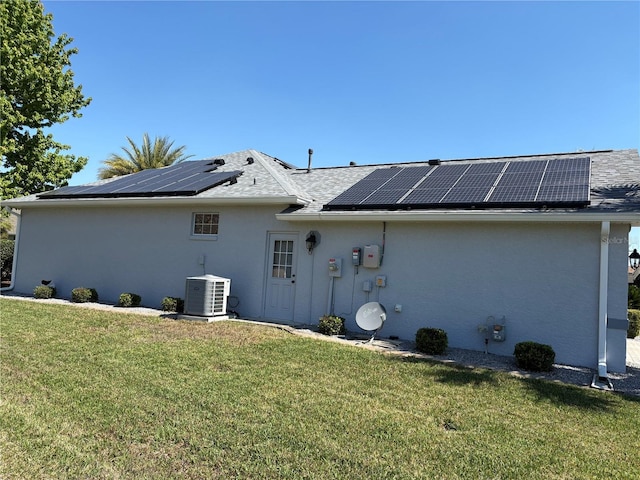 back of house with a lawn, central AC unit, solar panels, and stucco siding