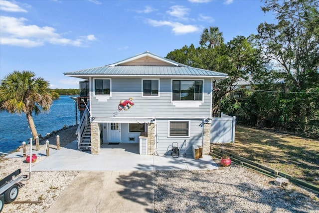 coastal home featuring stairs, metal roof, a water view, and a patio area