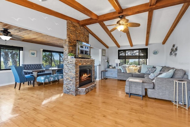 living room with light wood-style floors, ceiling fan, a stone fireplace, and high vaulted ceiling