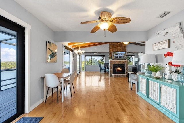 dining space featuring visible vents, light wood-style flooring, a stone fireplace, baseboards, and ceiling fan with notable chandelier