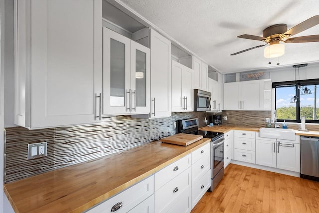 kitchen featuring stainless steel appliances, a sink, white cabinets, backsplash, and glass insert cabinets