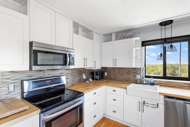 kitchen with open shelves, hanging light fixtures, appliances with stainless steel finishes, a sink, and butcher block countertops