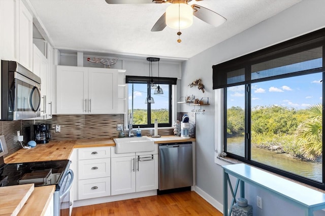 kitchen with hanging light fixtures, butcher block countertops, white cabinets, and stainless steel appliances