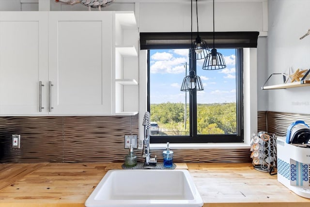 kitchen featuring wood finished floors, a sink, white cabinetry, backsplash, and pendant lighting