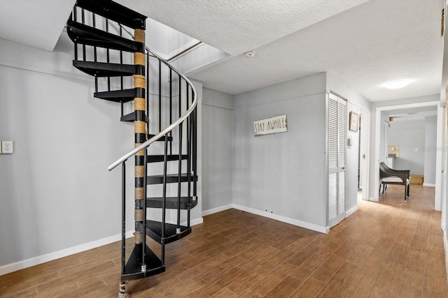 interior space with a textured ceiling, wood finished floors, and baseboards