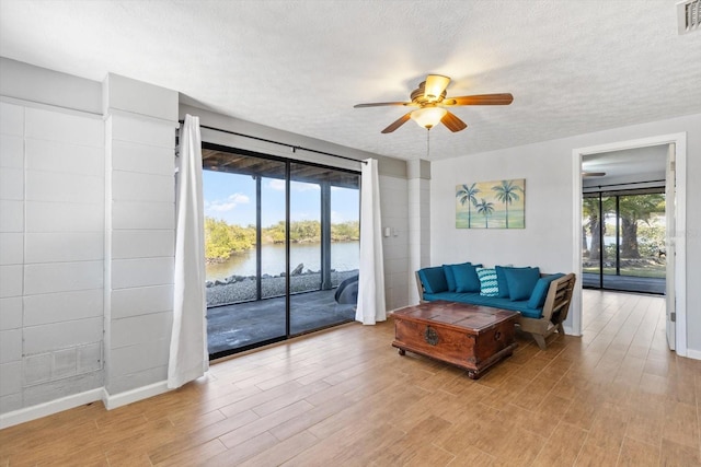 interior space featuring a textured ceiling, a water view, light wood-style flooring, and a ceiling fan