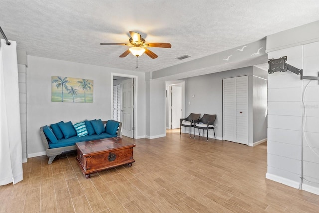 living area with a ceiling fan, visible vents, a textured ceiling, and wood finished floors