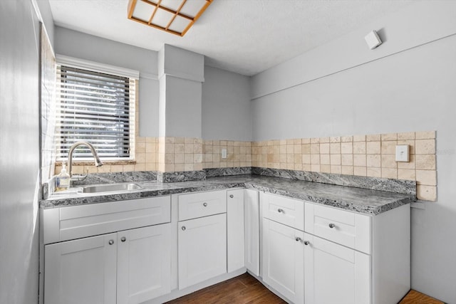 kitchen with white cabinets, dark countertops, dark wood-style flooring, a sink, and backsplash