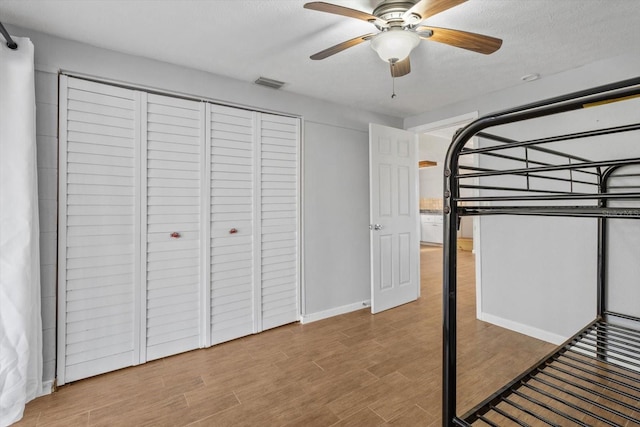 unfurnished bedroom with a closet, visible vents, ceiling fan, a textured ceiling, and wood finished floors