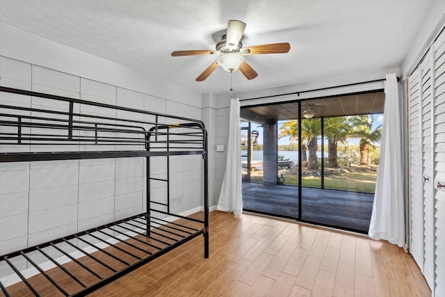 unfurnished bedroom with a textured ceiling, access to outside, ceiling fan, and wood finished floors