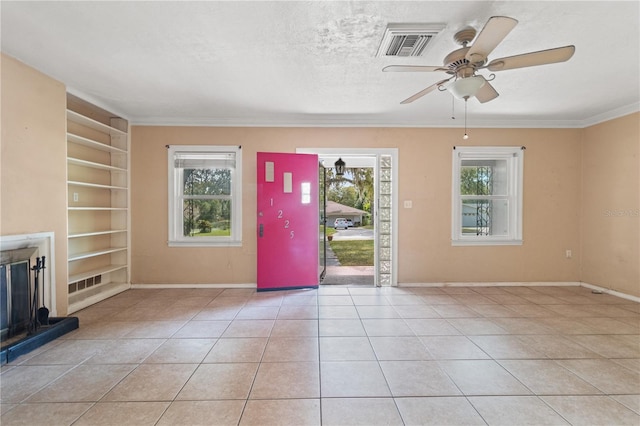 foyer featuring crown molding, visible vents, a glass covered fireplace, light tile patterned flooring, and a textured ceiling