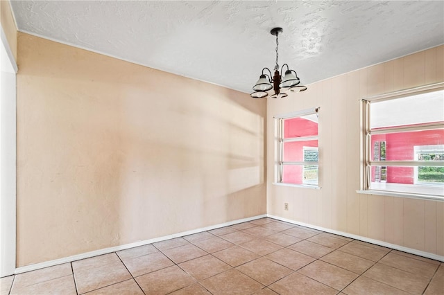 unfurnished room featuring a chandelier, wood walls, a textured ceiling, and tile patterned floors