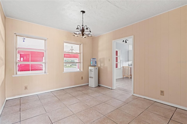 empty room with a chandelier, light tile patterned floors, a textured ceiling, and baseboards