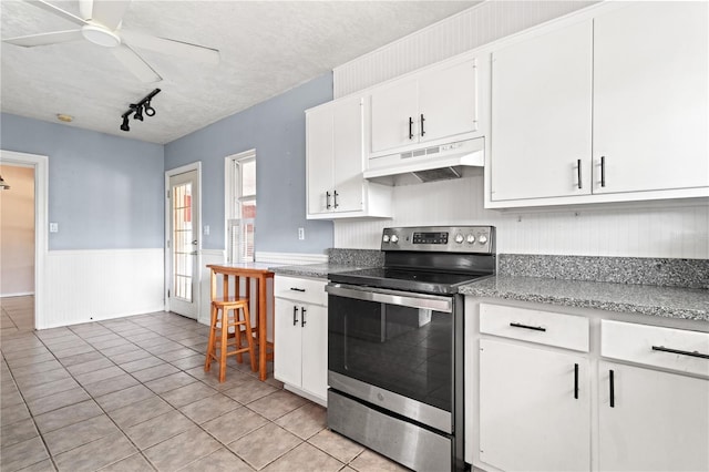 kitchen with under cabinet range hood, a wainscoted wall, electric range, a ceiling fan, and white cabinets