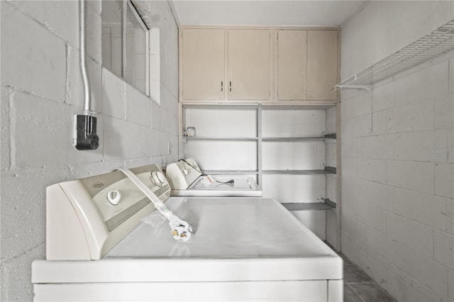 clothes washing area with concrete block wall, cabinet space, and washer and clothes dryer