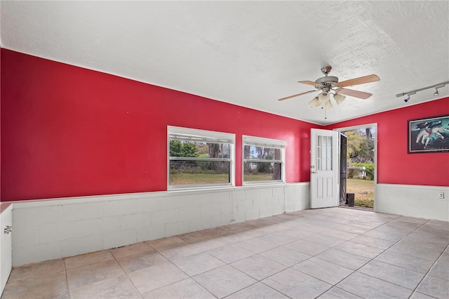 spare room featuring a textured ceiling, a wainscoted wall, light tile patterned flooring, and a ceiling fan