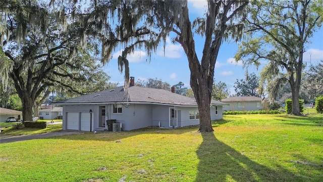 rear view of house featuring central AC, a lawn, an attached garage, and driveway