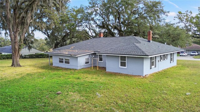 back of property with a shingled roof, a lawn, a chimney, and stucco siding