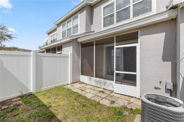 exterior space featuring a sunroom, fence, cooling unit, and stucco siding