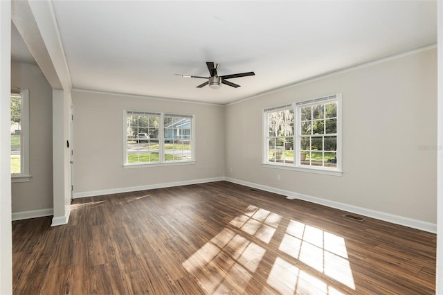 spare room with ornamental molding, dark wood-type flooring, a wealth of natural light, and baseboards