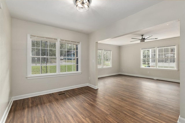 spare room with a ceiling fan, visible vents, baseboards, and dark wood-style flooring