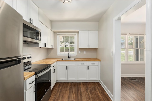 kitchen featuring appliances with stainless steel finishes, butcher block countertops, a sink, and white cabinetry