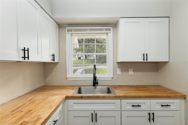 kitchen featuring wooden counters, a sink, and white cabinetry