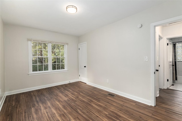 unfurnished room featuring dark wood-style floors, visible vents, and baseboards