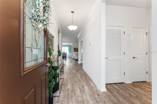 hall with light wood-type flooring, crown molding, and baseboards