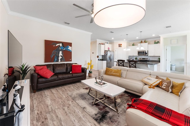 living room featuring light wood-style floors, visible vents, ornamental molding, and ceiling fan