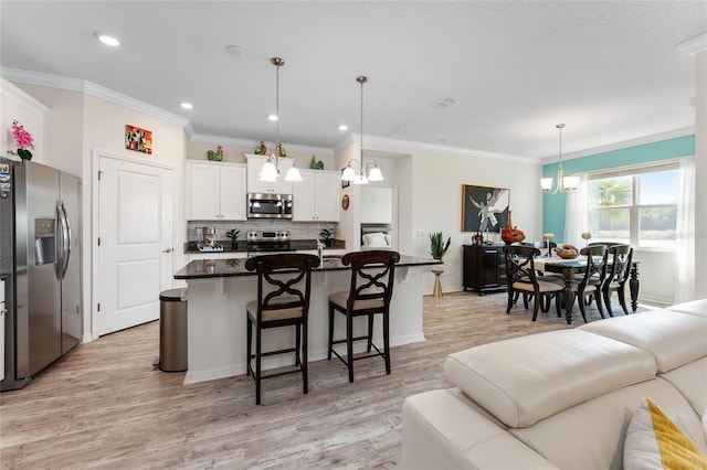 kitchen featuring light wood finished floors, appliances with stainless steel finishes, a breakfast bar, white cabinetry, and backsplash