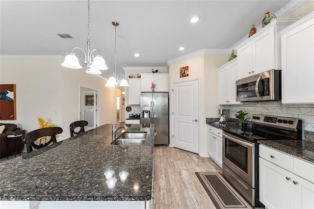 kitchen featuring visible vents, decorative backsplash, appliances with stainless steel finishes, a large island with sink, and a sink