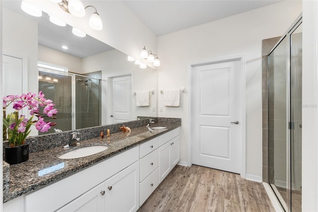 bathroom with double vanity, wood finished floors, a sink, and a shower stall