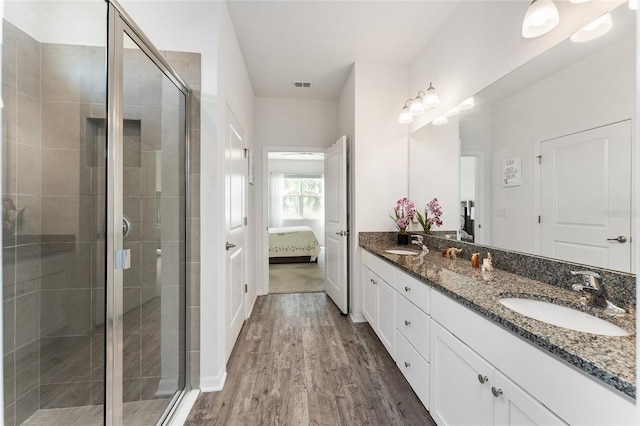 bathroom featuring connected bathroom, wood finished floors, a sink, a shower stall, and double vanity