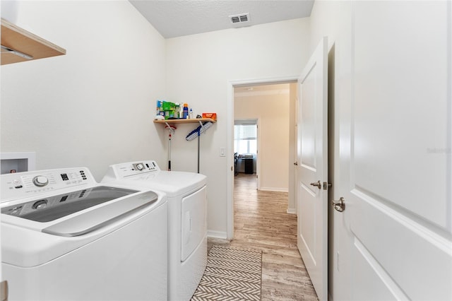 washroom with a textured ceiling, washing machine and dryer, light wood-style flooring, laundry area, and visible vents