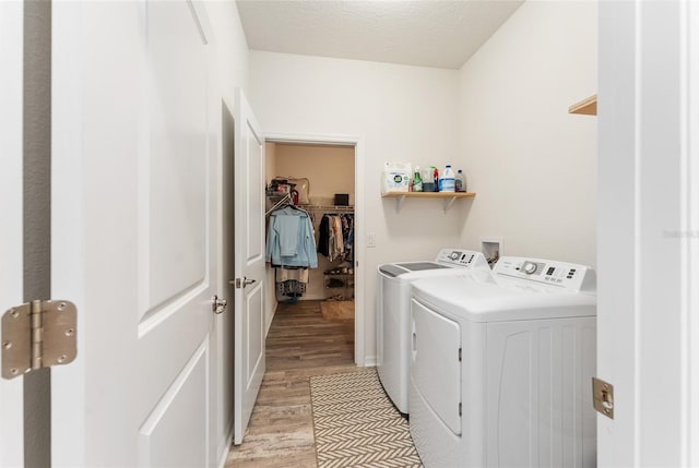 laundry area with a textured ceiling, laundry area, separate washer and dryer, and light wood-style floors