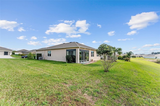 rear view of property featuring central air condition unit, a lawn, and stucco siding