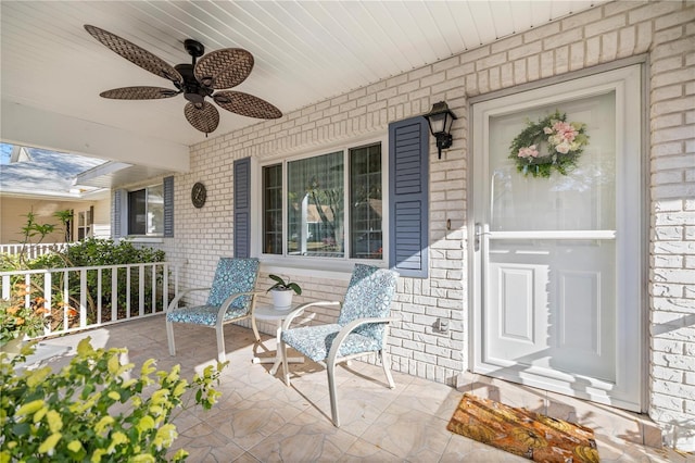 view of exterior entry with brick siding, covered porch, and ceiling fan