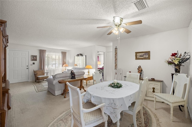 dining area with a textured ceiling, light carpet, visible vents, and ceiling fan