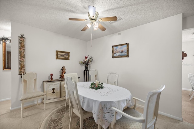 dining space featuring light carpet, a ceiling fan, baseboards, and a textured ceiling