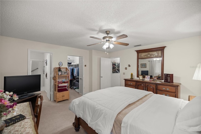 bedroom with a ceiling fan, a closet, a textured ceiling, a walk in closet, and light colored carpet