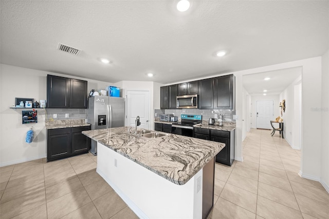 kitchen featuring a center island with sink, visible vents, appliances with stainless steel finishes, light stone countertops, and a sink