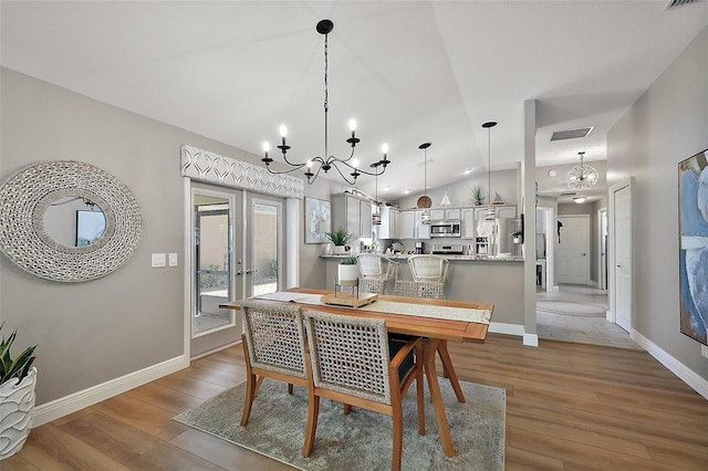 dining area with baseboards, visible vents, light wood-style flooring, vaulted ceiling, and a notable chandelier