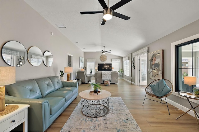 living area featuring lofted ceiling, a textured ceiling, a ceiling fan, visible vents, and light wood-style floors