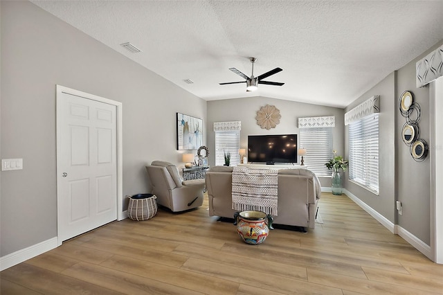 living area with a ceiling fan, light wood-type flooring, visible vents, and vaulted ceiling