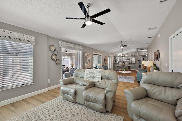 living room featuring light wood-style floors, lofted ceiling, ceiling fan, and a textured ceiling