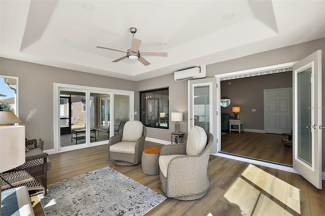 sitting room featuring baseboards, a raised ceiling, wood finished floors, an AC wall unit, and french doors