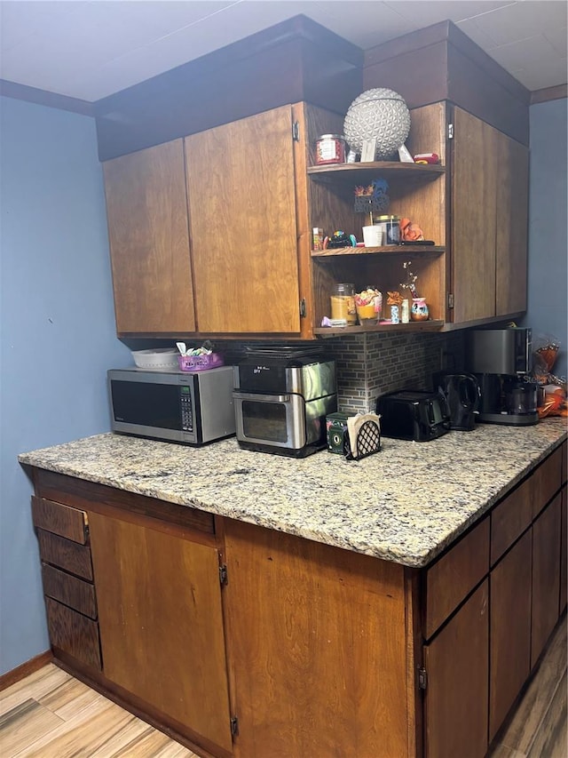 kitchen with light stone counters, stainless steel microwave, light wood finished floors, decorative backsplash, and baseboards