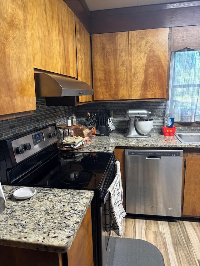 kitchen with under cabinet range hood, stainless steel appliances, brown cabinets, and decorative backsplash