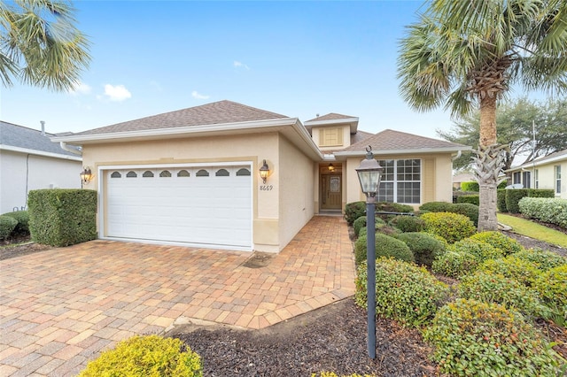 view of front of property featuring a garage, decorative driveway, a shingled roof, and stucco siding